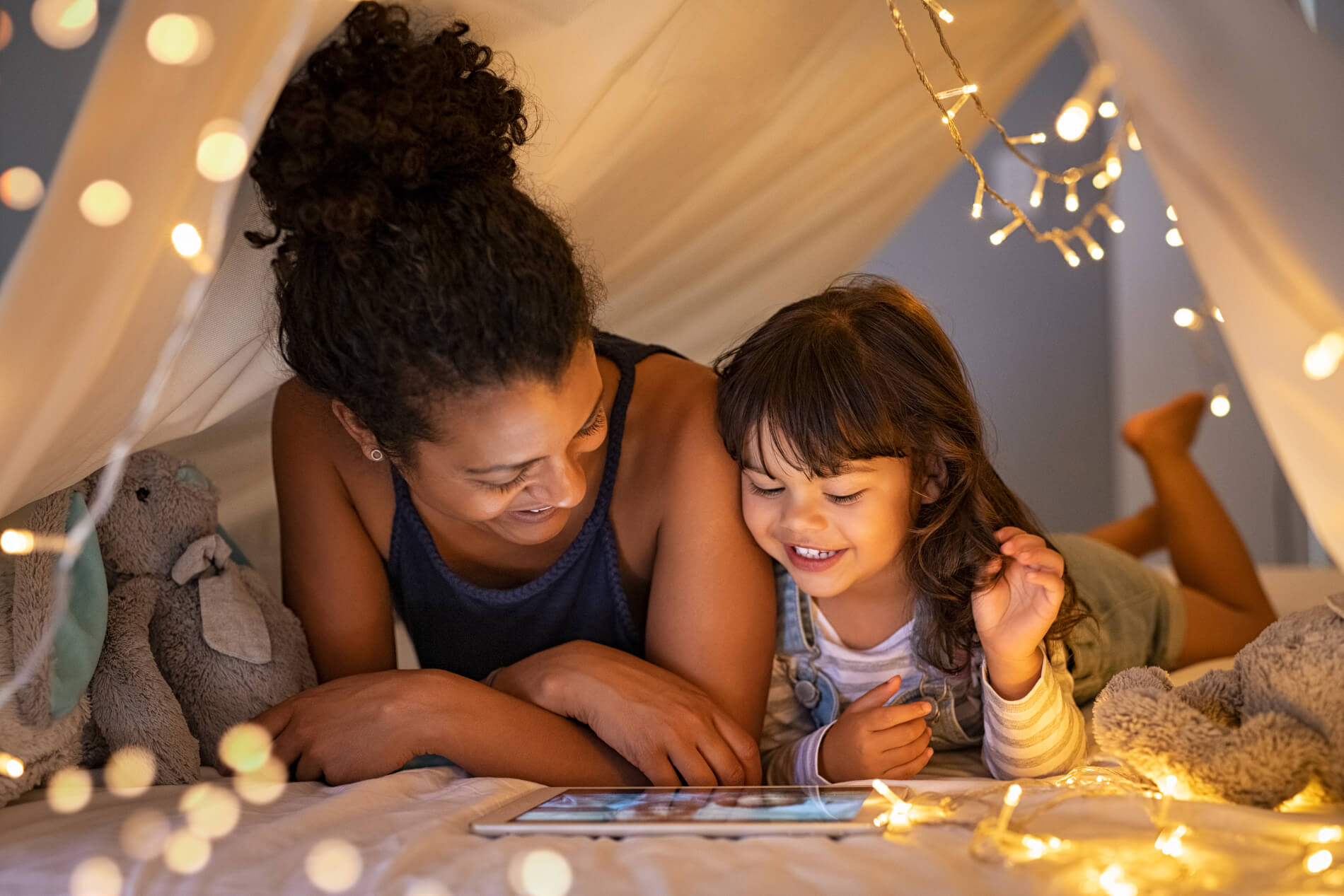 Mother and child watching a movie on an iPad under the lights of a play tent